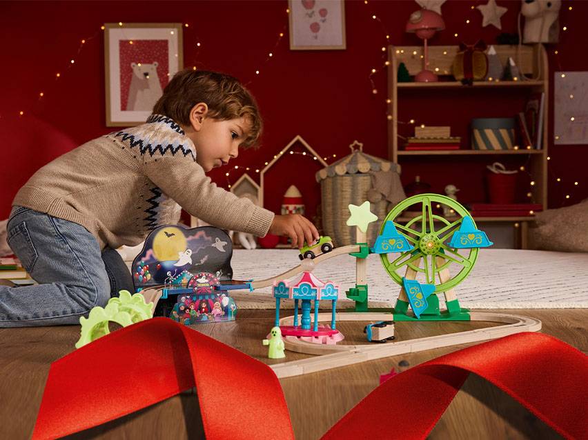 Kind spielt mit einer Holzeisenbahn und einem Riesenrad auf dem Boden.
