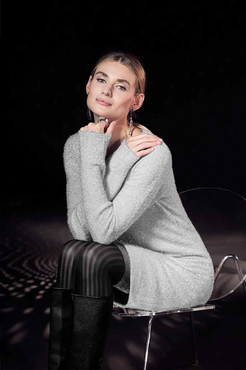 Frau in glitzerndem Strickkleid und gestreiften Strumpfhosen auf einem Stuhl sitzend