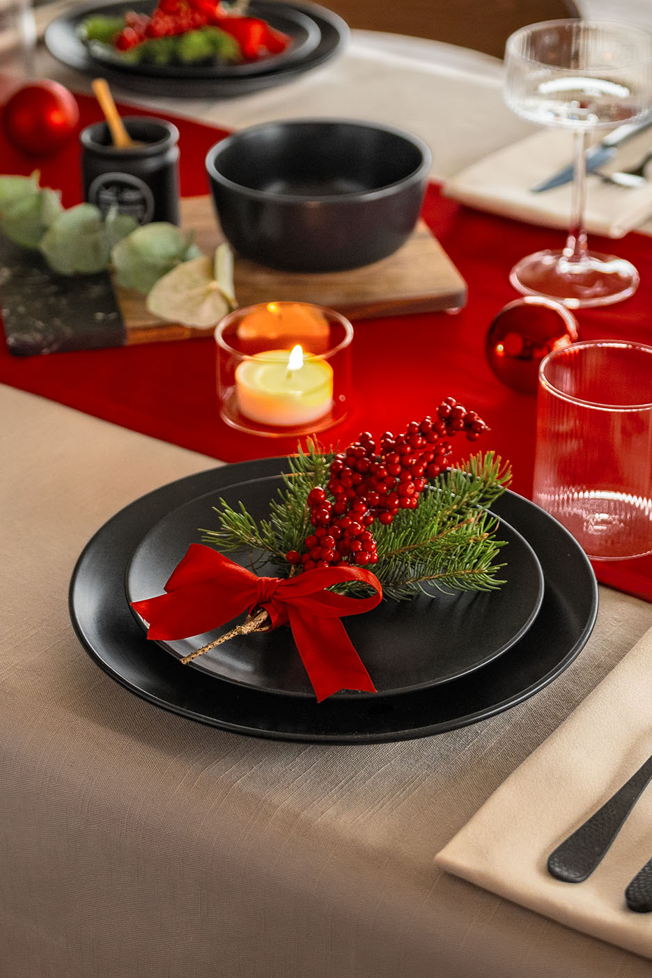 Festlich gedeckter Tisch mit rotem Läufer, schwarzen Tellern, Gläsern und Kerzen.