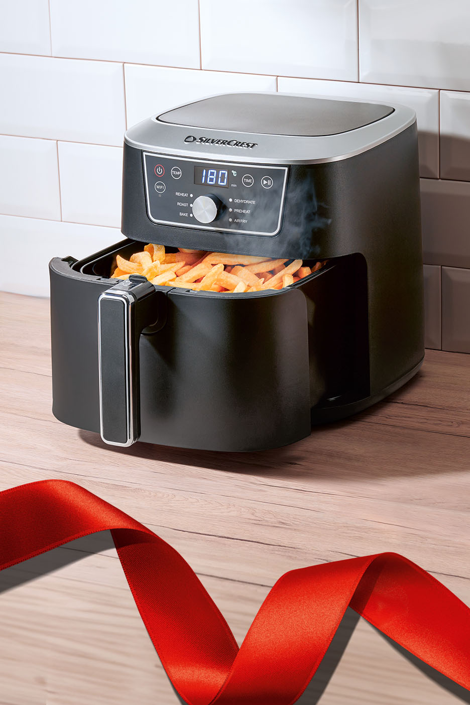 SilverCrest Heißluftfritteuse mit Pommes frites und rotem Band auf Holztisch