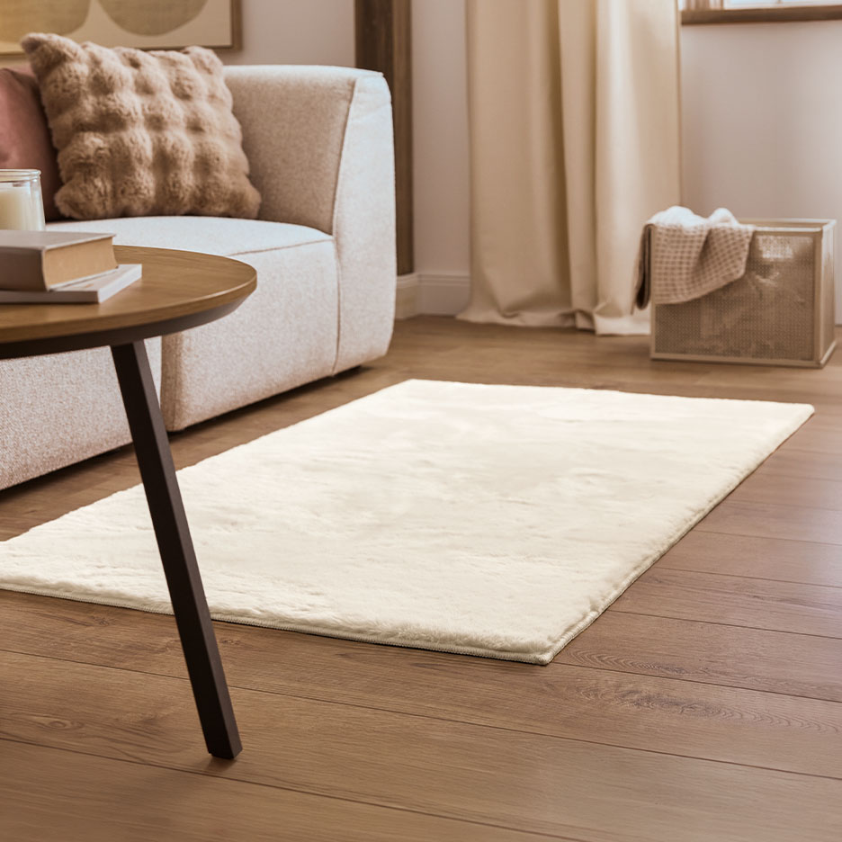 Cremefarbener Teppich auf Holzboden vor einem Sofa und Beistelltisch