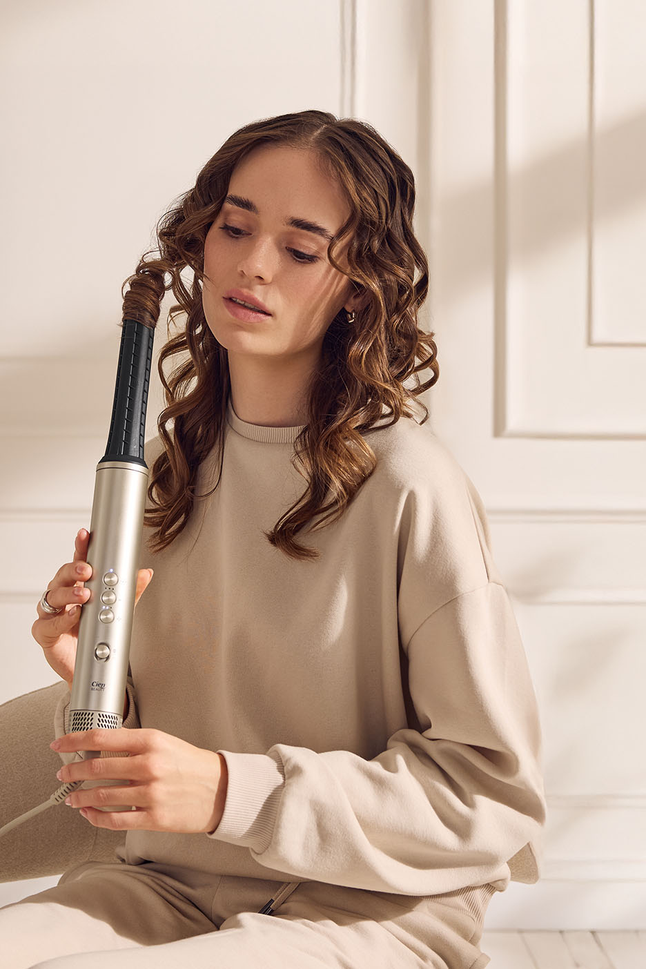 Junge Frau mit lockigem Haar, die einen goldenen Lockenstab hält.