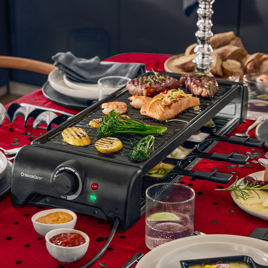 SilverCrest Raclette-Grill mit Fleisch, Fisch und Gemüse auf einem festlich gedeckten Tisch.