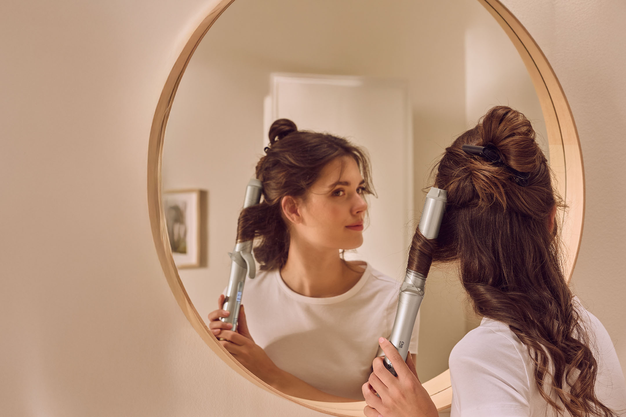 Frau lockt sich die Haare mit einem Cien Beauty Lockenstab vor einem Spiegel.