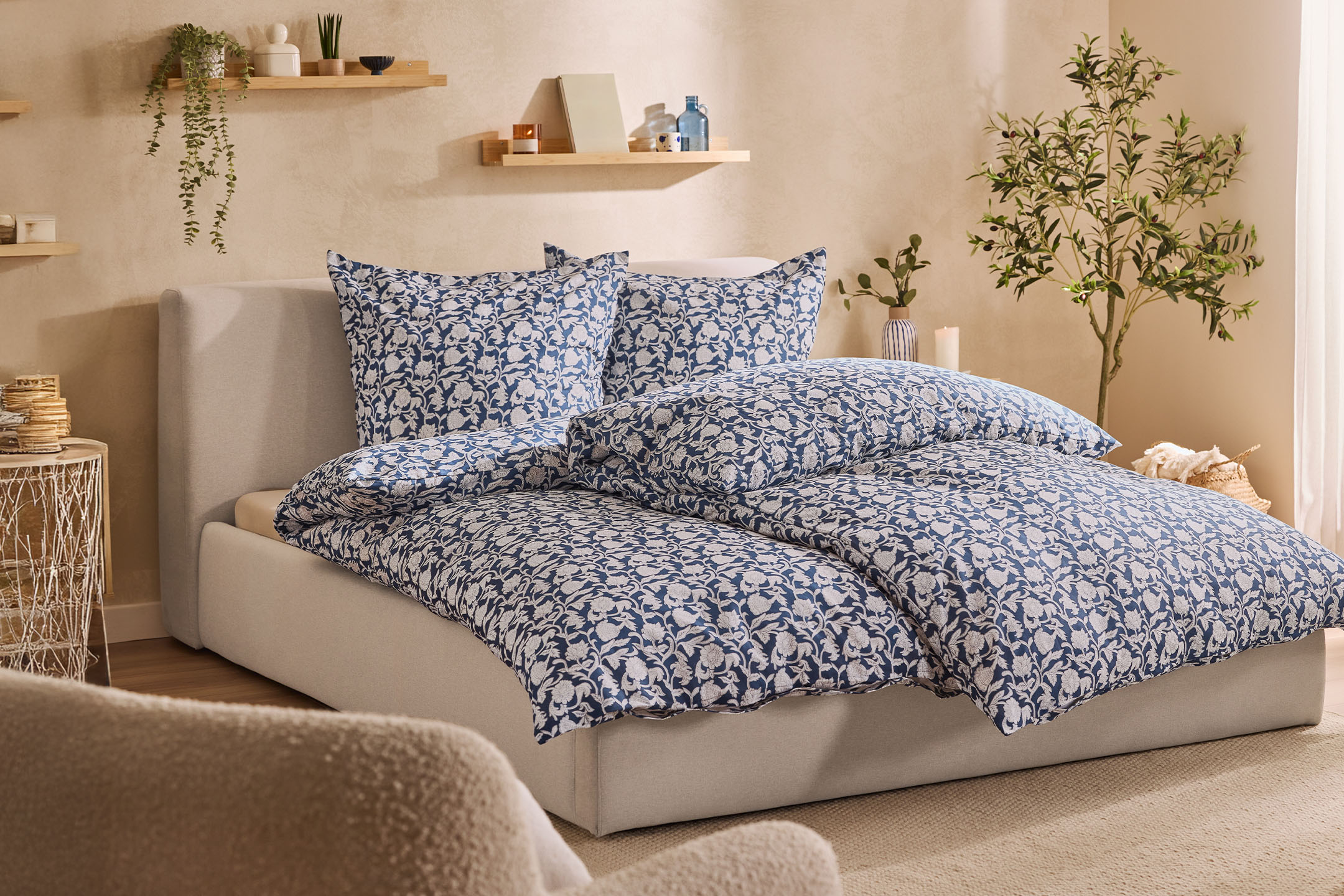 Schlafzimmer mit Bett in Beige und blauer Bettwäsche mit Blumenmuster, Wandregale mit Pflanzen