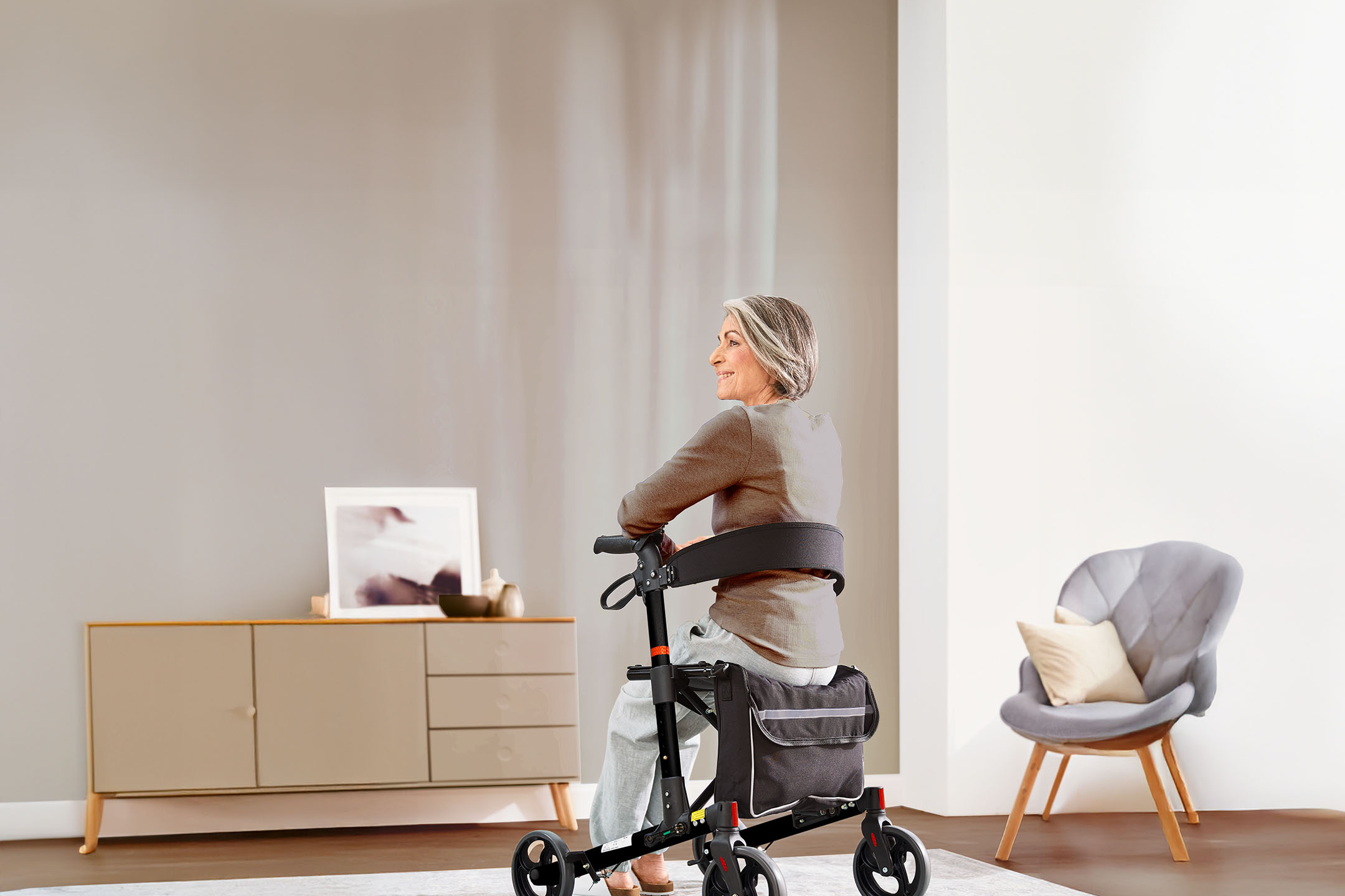 Ältere Frau sitzt auf einem Rollator in einem modernen Wohnzimmer.