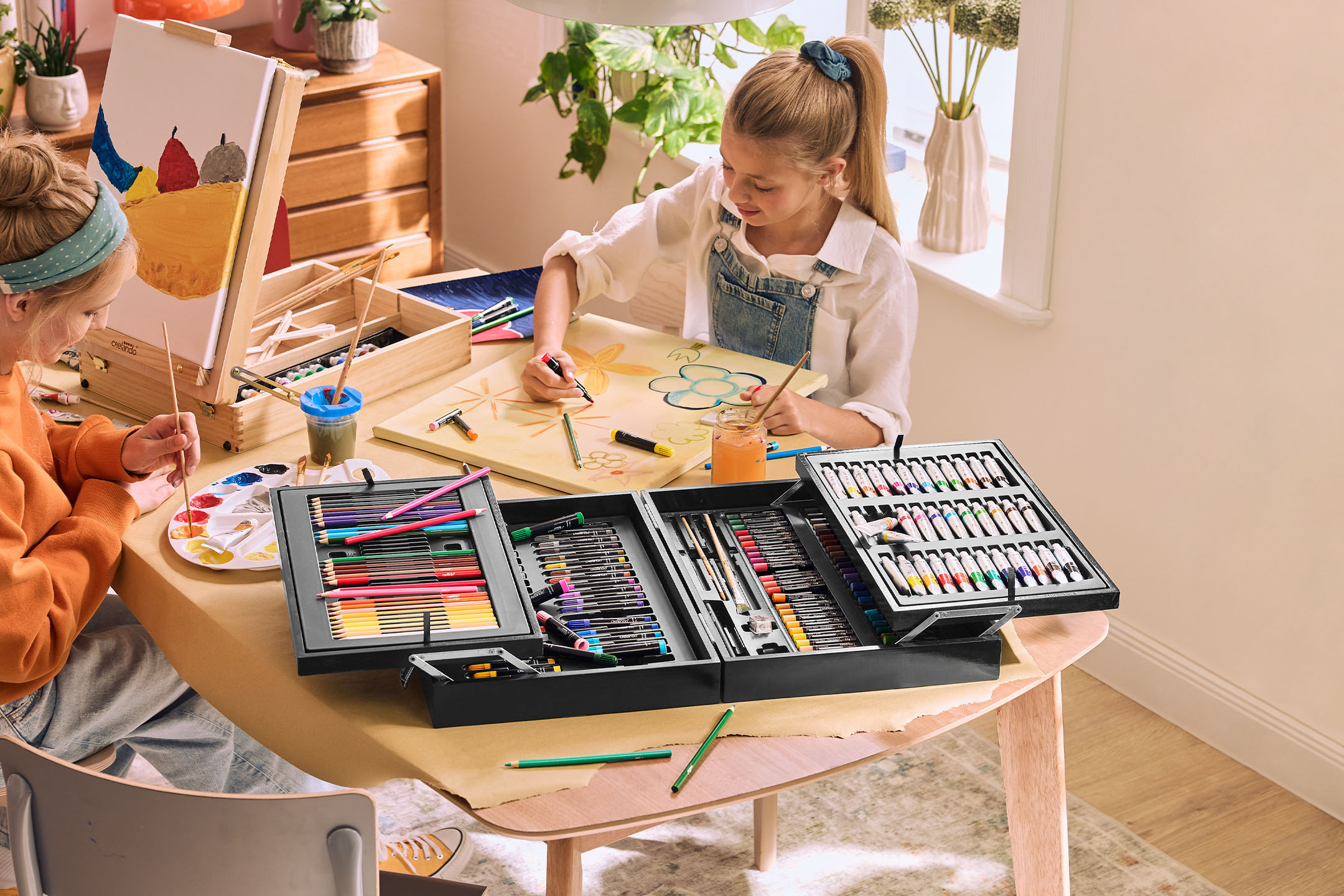 Zwei Kinder malen mit einem großen Malset, das Buntstifte, Marker, Ölpastelle und Acrylfarben enthält.