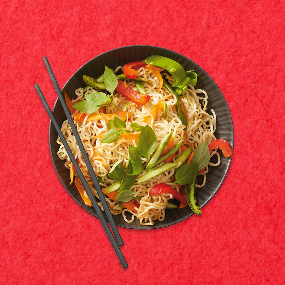 Nudeln mit Gemüse und Basilikum in einer schwarzen Schale mit Essstäbchen