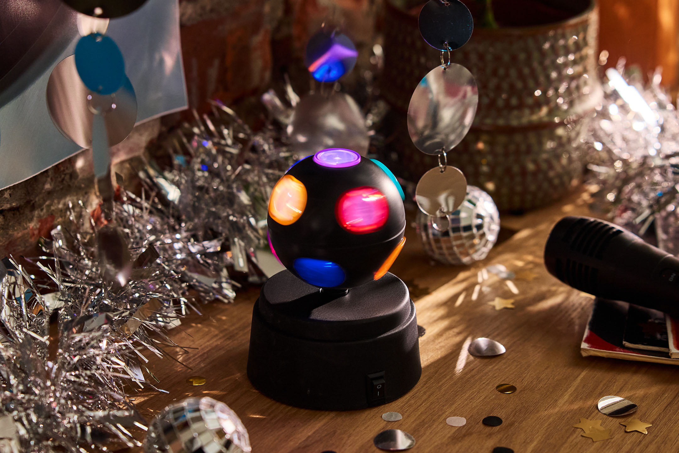 Bunte Disco-Lichtkugel und Mikrofon auf einem Holztisch mit Partydekoration.