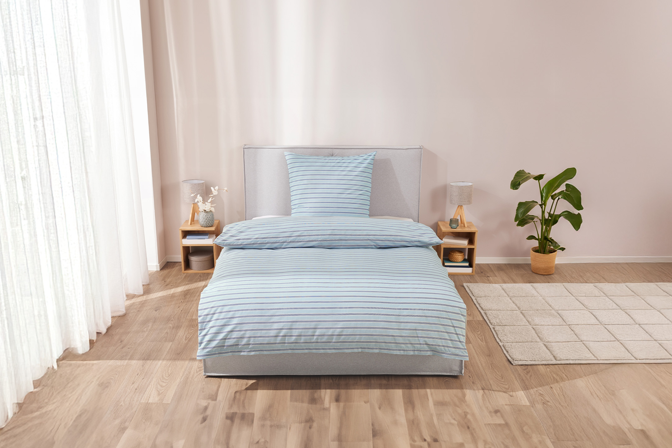 Schlafzimmer mit Bettwäsche in Blau- und Weißtönen, Holzboden und hellem Teppich.