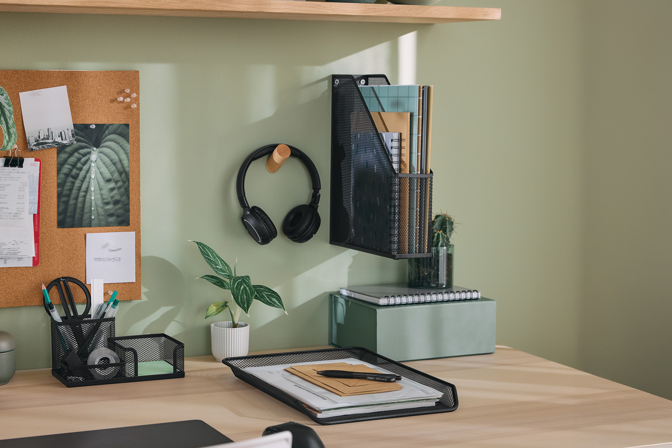 Schreibtisch mit schwarzem Organizer, Kopfhörern, Pflanzen und Notizbüchern.