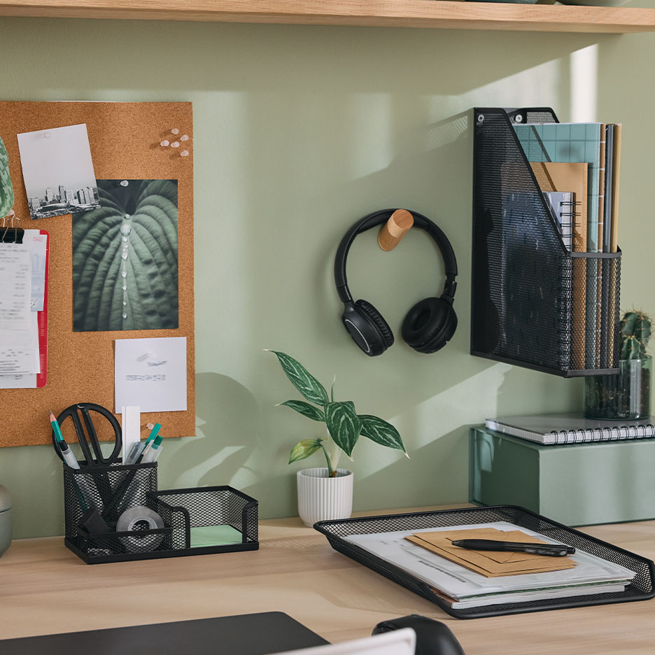 Schreibtisch mit schwarzem Organizer, Kopfhörern und Pinnwand.