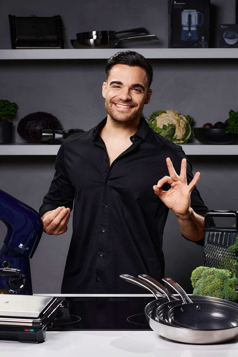 Lächelnder Koch mit Küchengeräten, Pfannen und frischem Gemüse