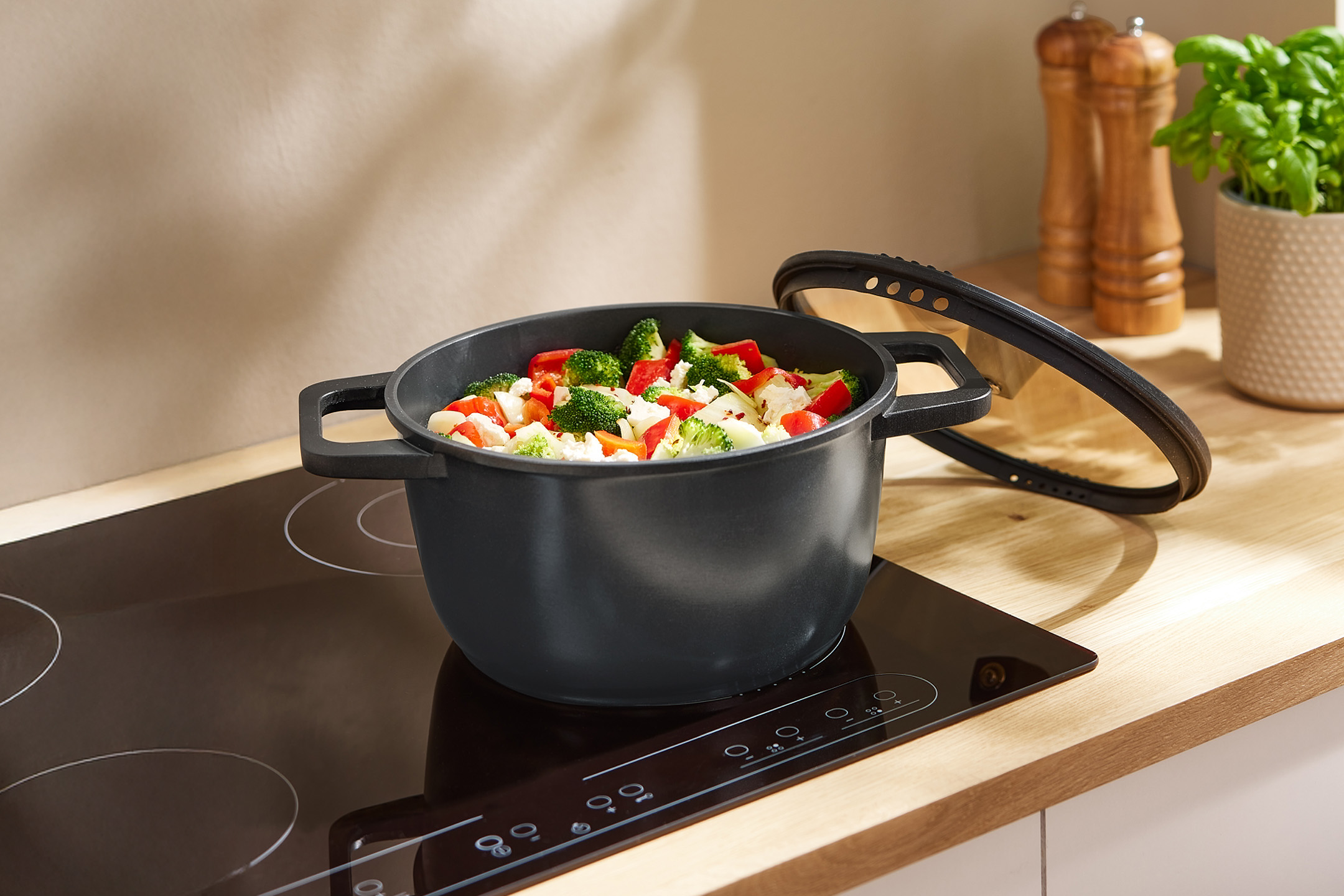 Schwarzer Topf mit Gemüse auf einem Induktionskochfeld in einer modernen Küche.