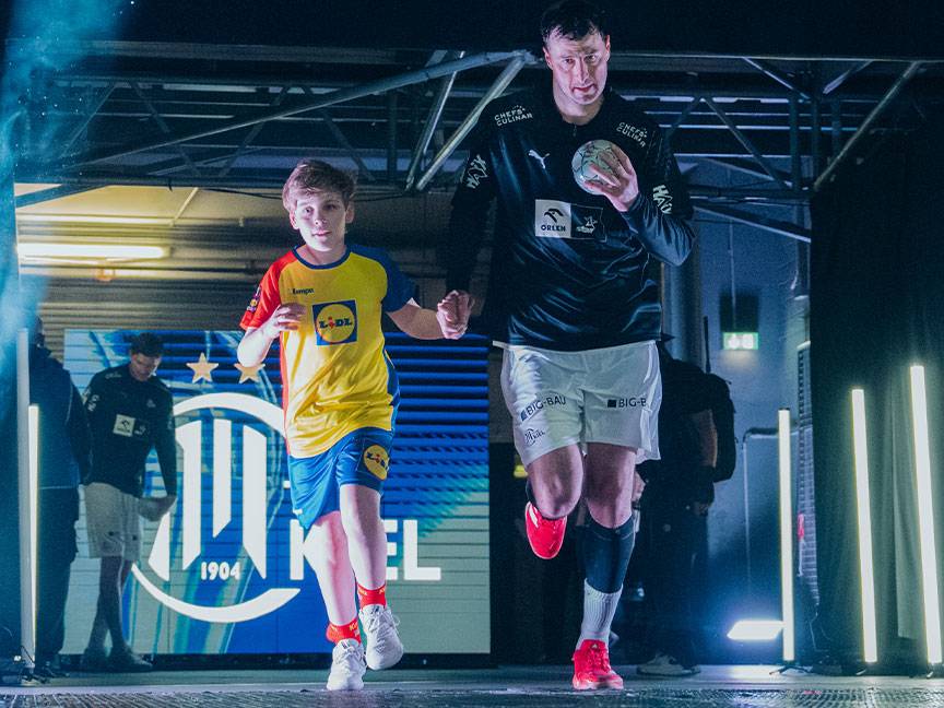 Ein Kind und ein Erwachsener in Sportkleidung, das Kind trägt ein Lidl-T-Shirt, laufen aus einem Tunnel.