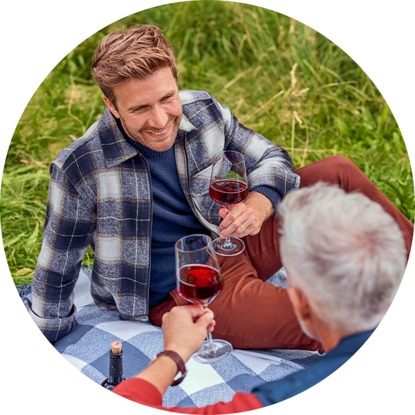 Zwei Männer genießen Rotwein bei einem Picknick im Freien.