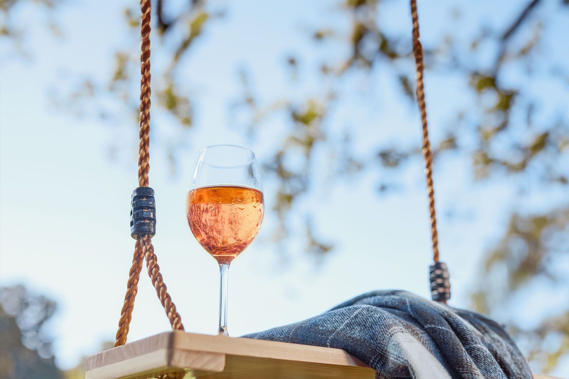 Roséwein in einem Glas auf einer Holzschaukel mit einer Decke, im Freien.