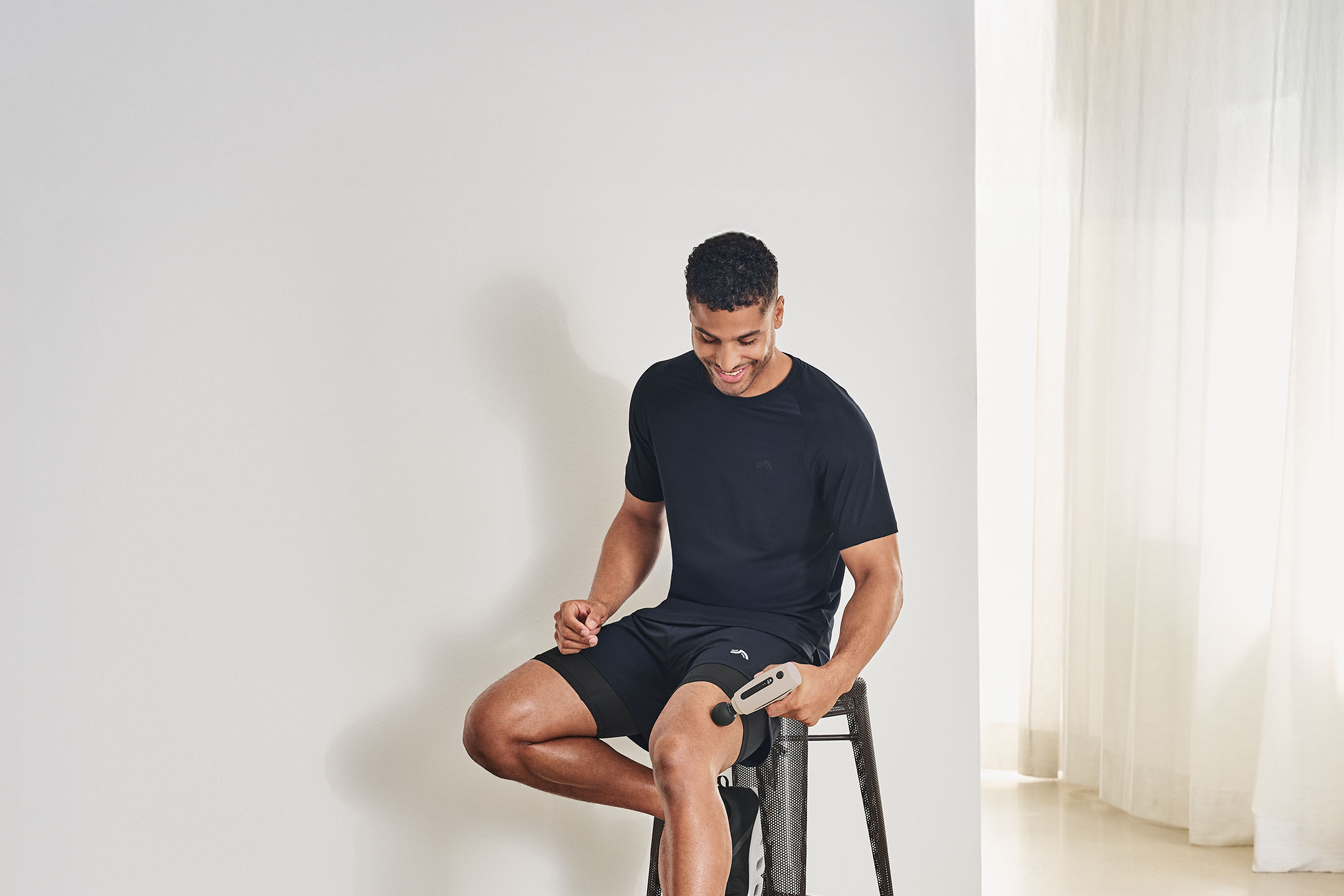 Mann in Sportkleidung massiert seinen Oberschenkel mit einem Massagegerät.