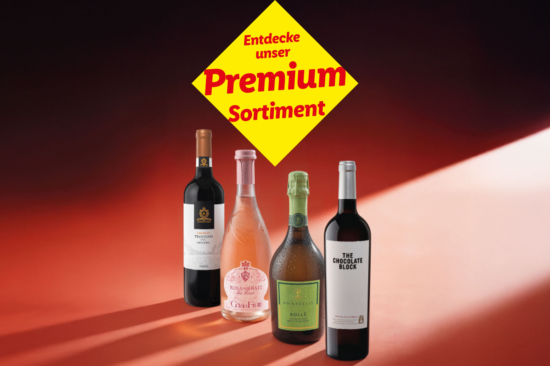 Vier Flaschen Wein und Sekt auf rotem Hintergrund mit dem Text „Entdecke unser Premium Sortiment“.
