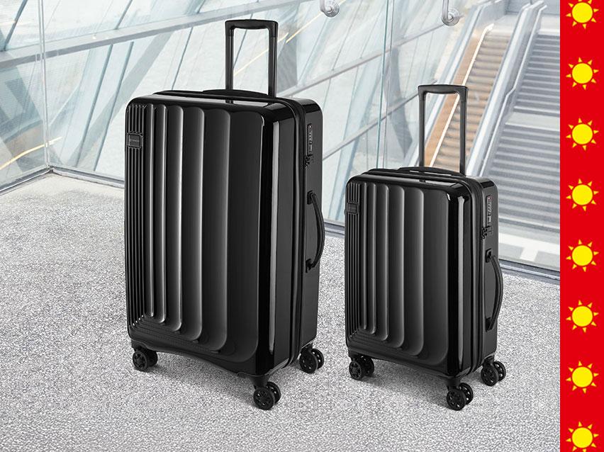 Zwei schwarze Rollkoffer in einem modernen Flughafen- oder Bahnhofsgebäude.