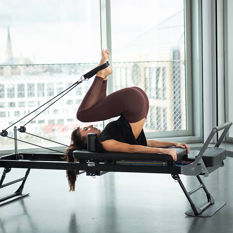 Frau macht Pilates auf einem Reformer mit Beinen oben und Füßen in Schlaufen.