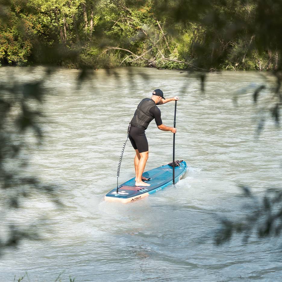 Mann in Neoprenanzug und Schwimmweste paddelt auf blauem SUP-Board auf einem Fluss.