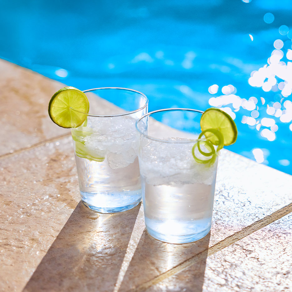 Zwei Gläser mit Eiswasser und Limettenscheiben am Poolrand