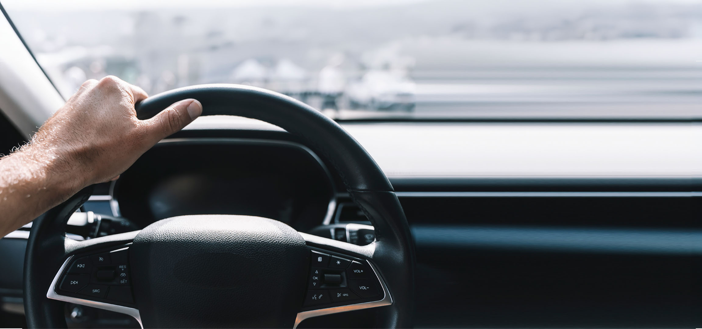 Männerhand hält das Lenkrad eines Autos.