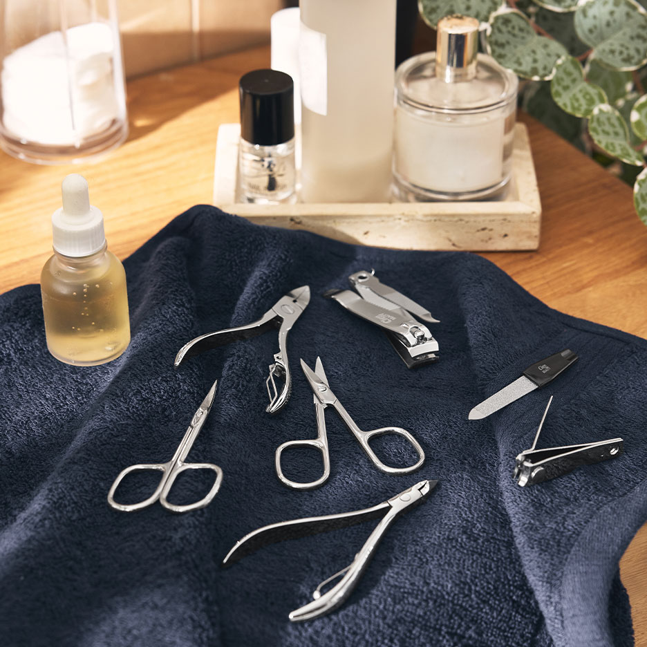 Maniküre-Set mit Nagelknipsern, Scheren und Feilen auf einem dunkelblauen Handtuch.