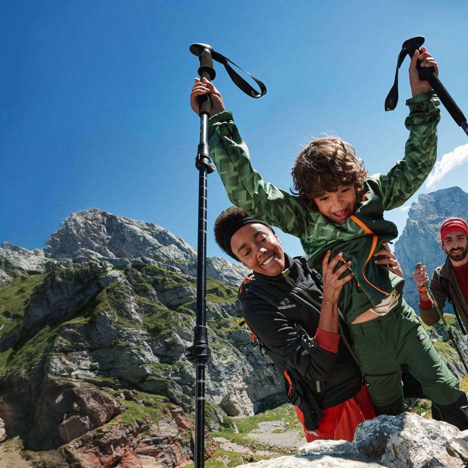 Familie wandert mit Trekkingstöcken und Outdoor-Kleidung in den Bergen.