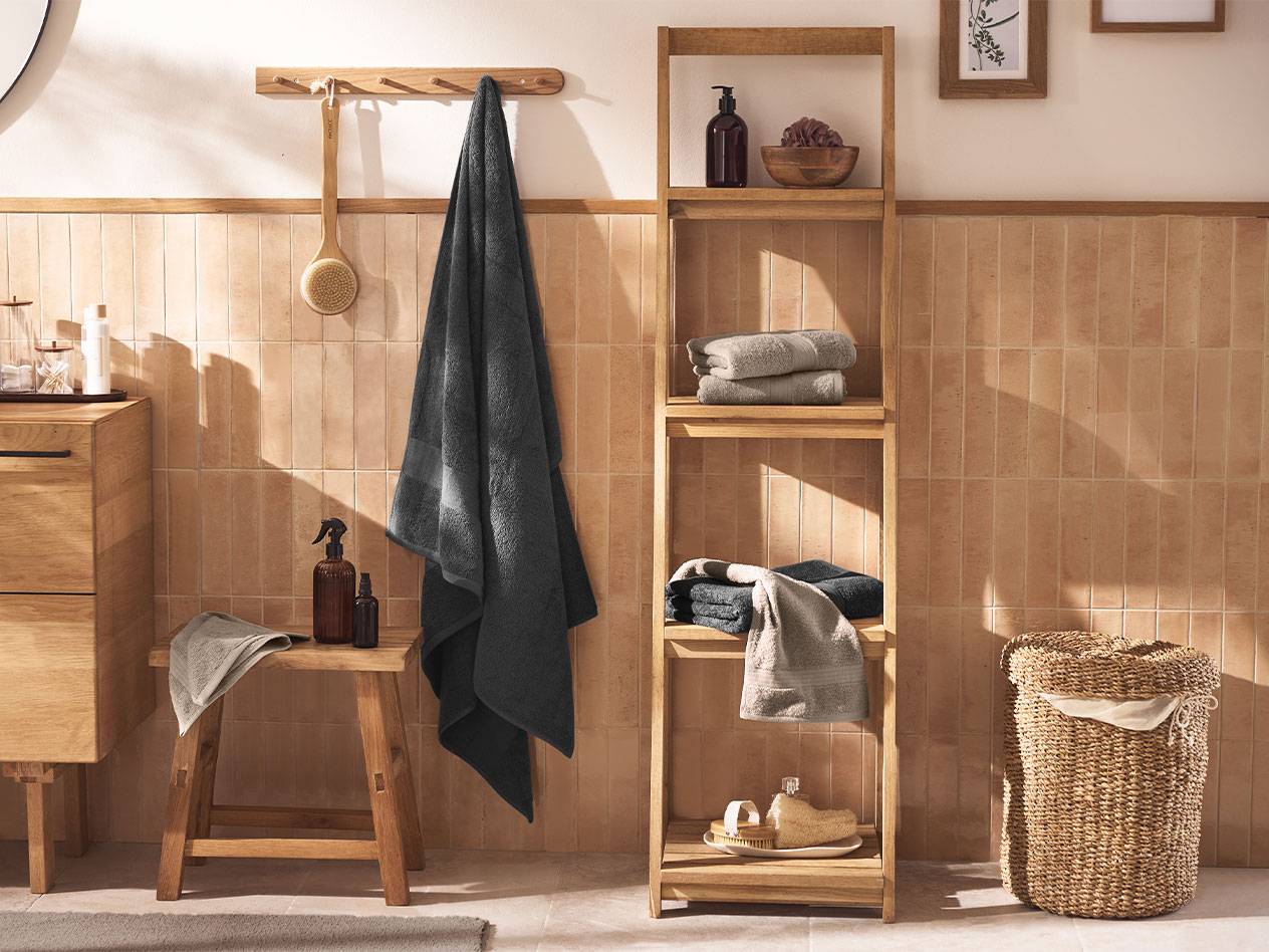 Badezimmer mit grauen Handtüchern, Holzregalen und Badaccessoires.