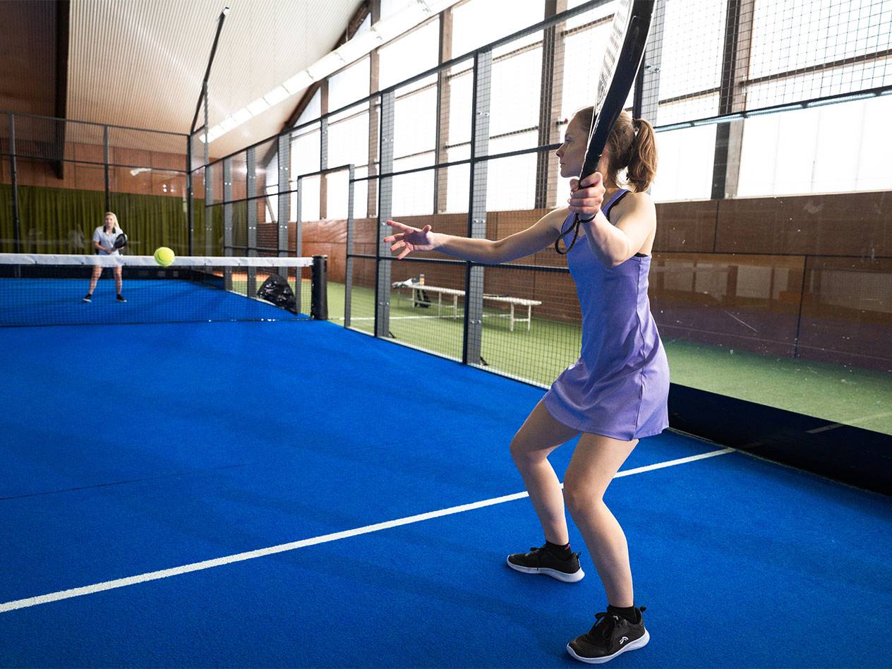 Frau im lila Kleid spielt Padel auf einem blauen Platz.