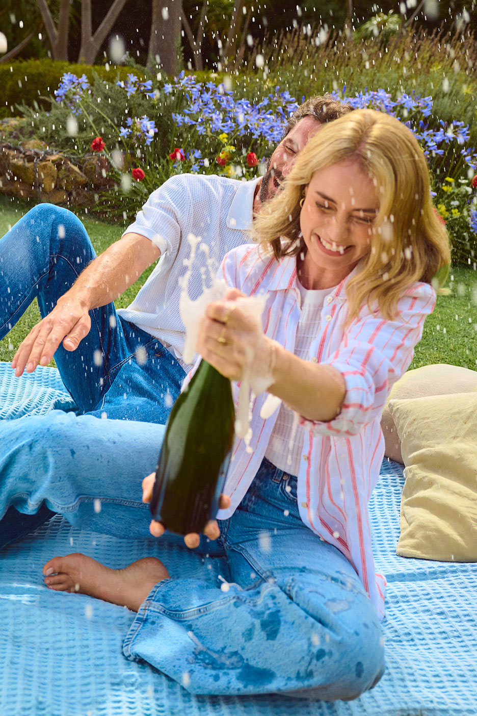 Fröhliches Paar feiert mit Sekt im Freien, umgeben von Blumen.