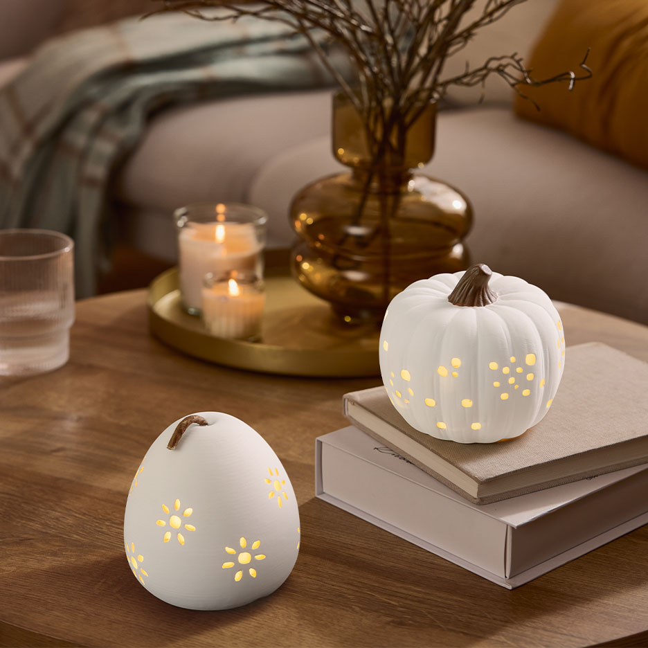 Zwei weiße beleuchtete Deko-Kürbisse auf einem Holztisch mit Kerzen und einer Vase.