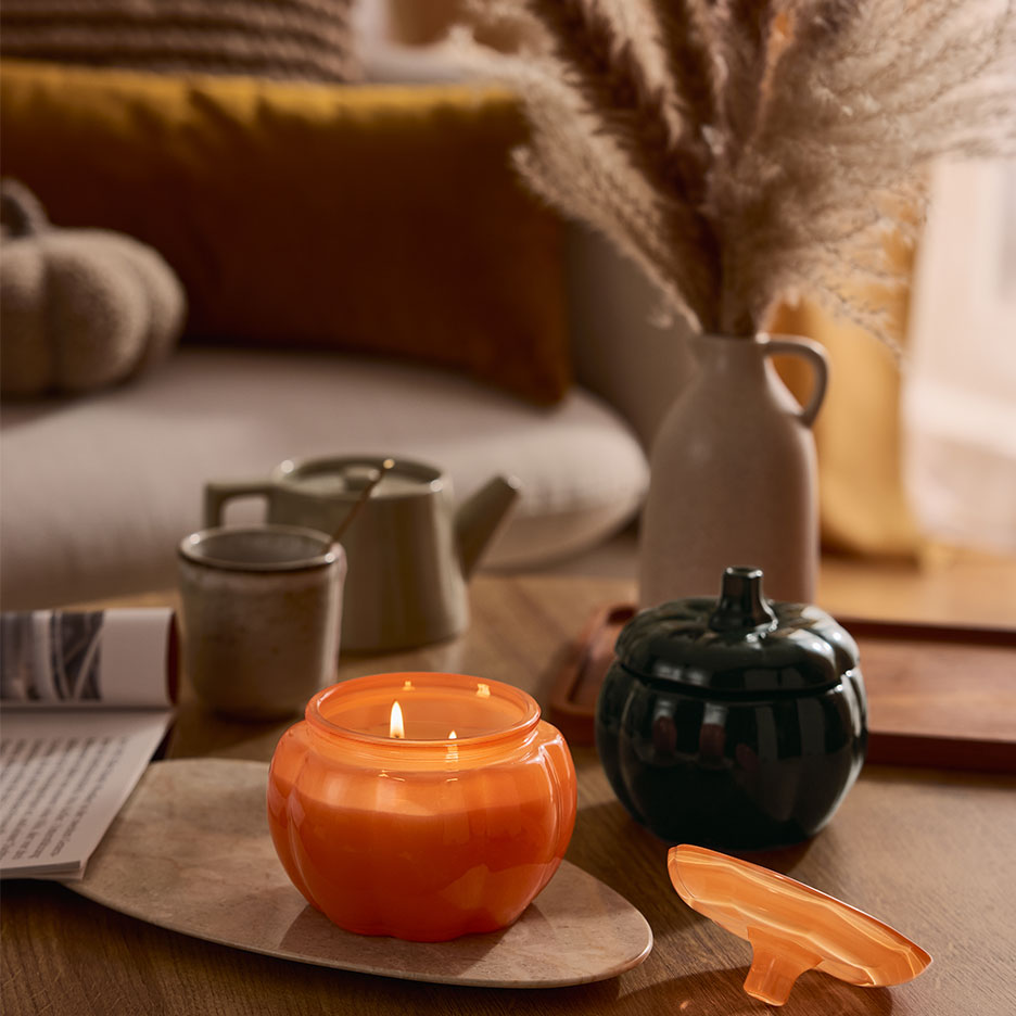 Kürbisförmige Kerze und Behälter auf einem Couchtisch mit Herbstdekoration.