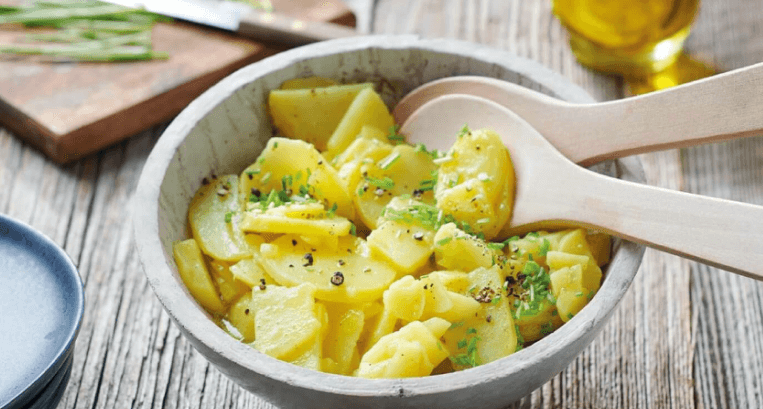 Kartoffelsalat mit Schnittlauch und Pfeffer in einer Holzschale mit Holzlöffeln