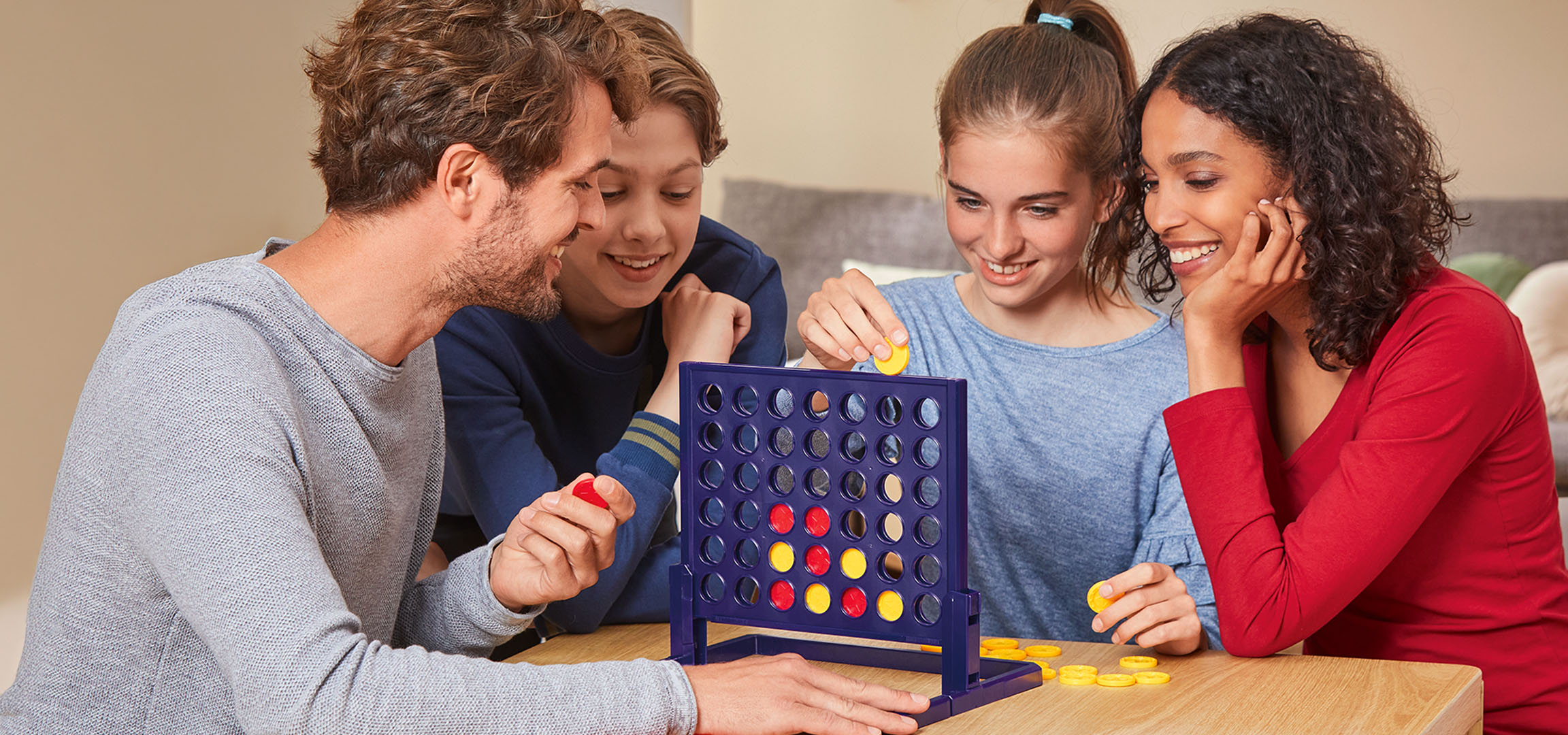 Vier Personen spielen das Brettspiel Connect 4 an einem Holztisch.