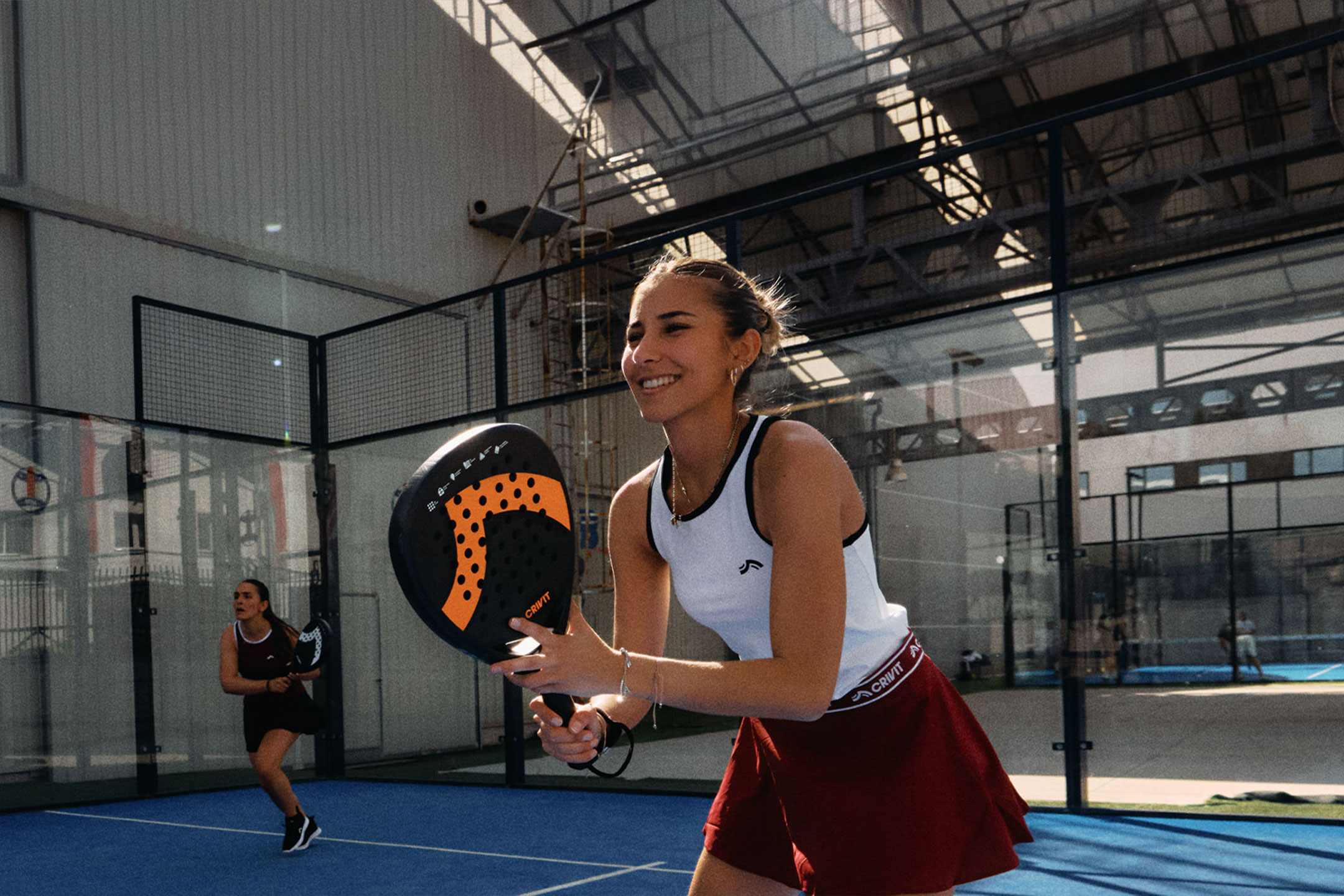 AI-generiert: Zwei Frauen spielen Padel-Tennis, eine lächelt und hält einen Schläger, auf einem blauen Platz.