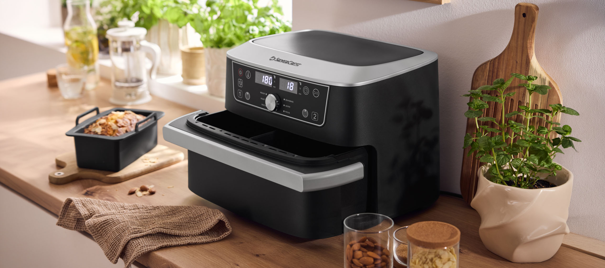 Schwarze Heißluftfritteuse mit Doppelofen und Gebäck auf einer Holztheke.