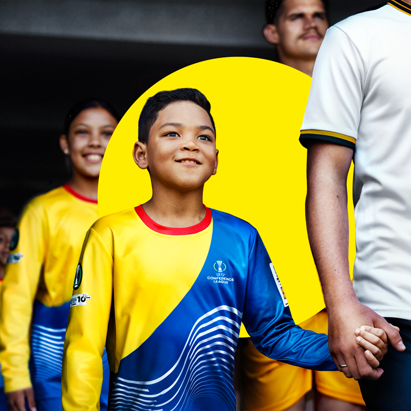Ein kleiner Junge in einem gelb-blauen Fußballtrikot hält die Hand eines Erwachsenen.