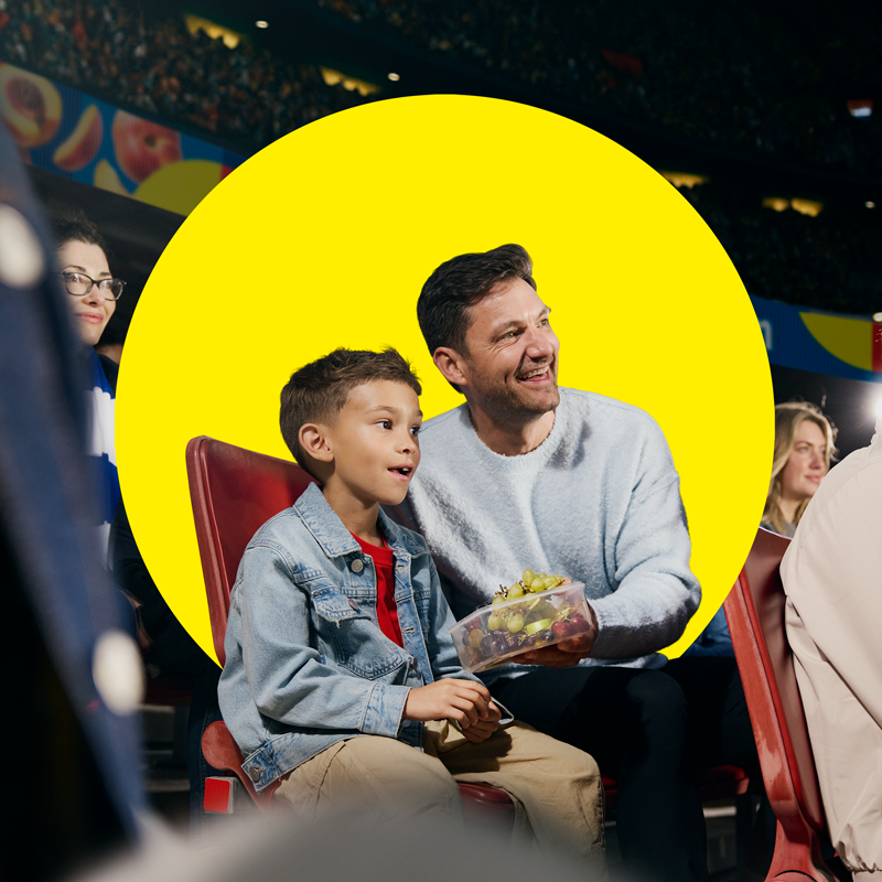 Vater und Sohn genießen Obst in einem Behälter bei einem Sportereignis.