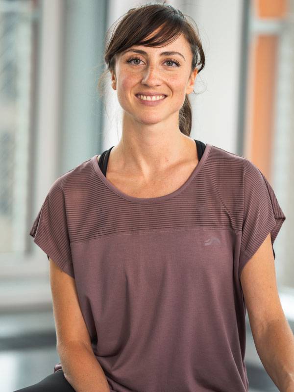 Lächelnde Frau in einem kurzärmeligen lila Sporttop.