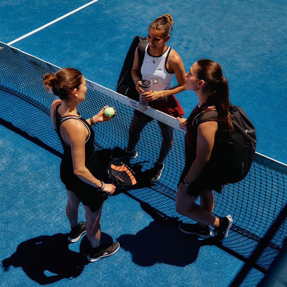 Agostina Bigotti und zwei Mitspielerinnen in CRIVIT Sportbekleidung stehen nach dem Spiel zusammen am Padel-Netz auf einem blauen Court.