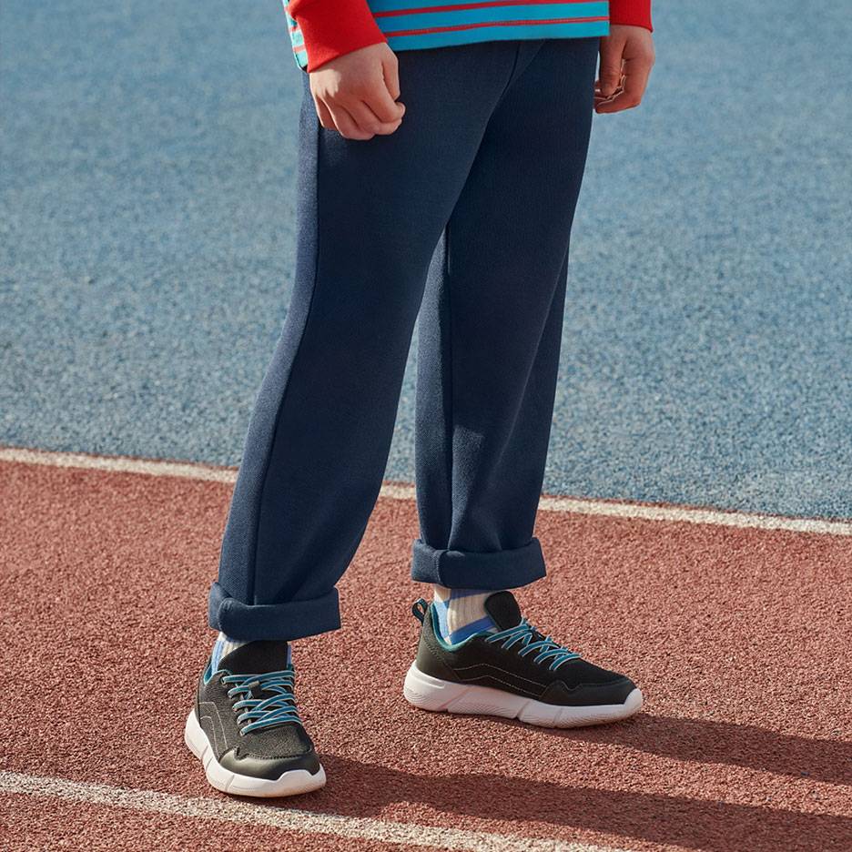 Dunkelblaue Jogginghose und schwarze Sneaker mit blauen Schnürsenkeln auf einer Laufbahn.