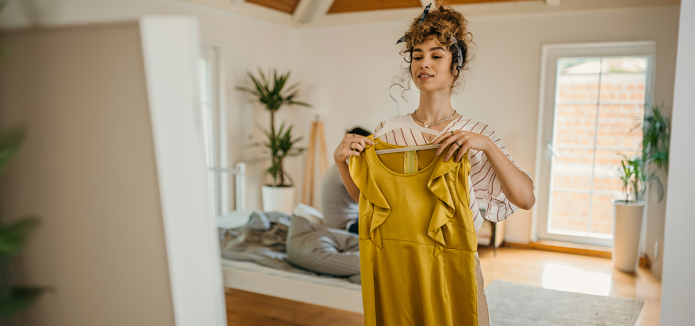 Frau hält ein gelbes Kleid an einem Kleiderbügel im Schlafzimmer.