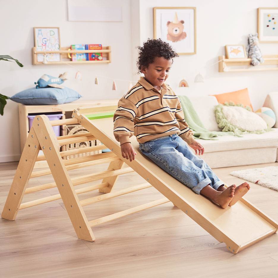 Kind spielt auf einer Holzrutsche und Leiter in einem Kinderzimmer.
