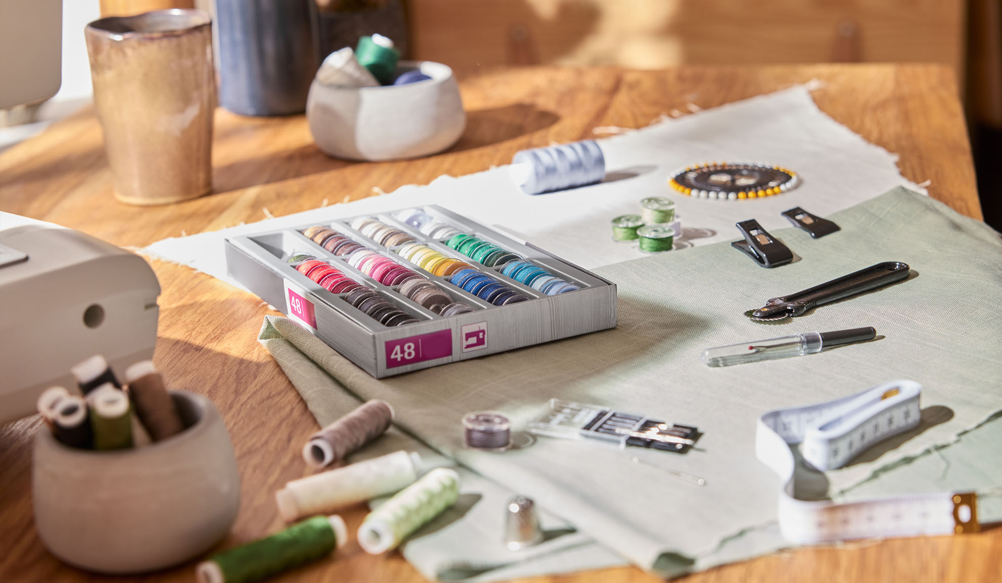 Nähset mit einer Box bunter Garne, Nähmaschine und verschiedenen Werkzeugen auf einem Holztisch.