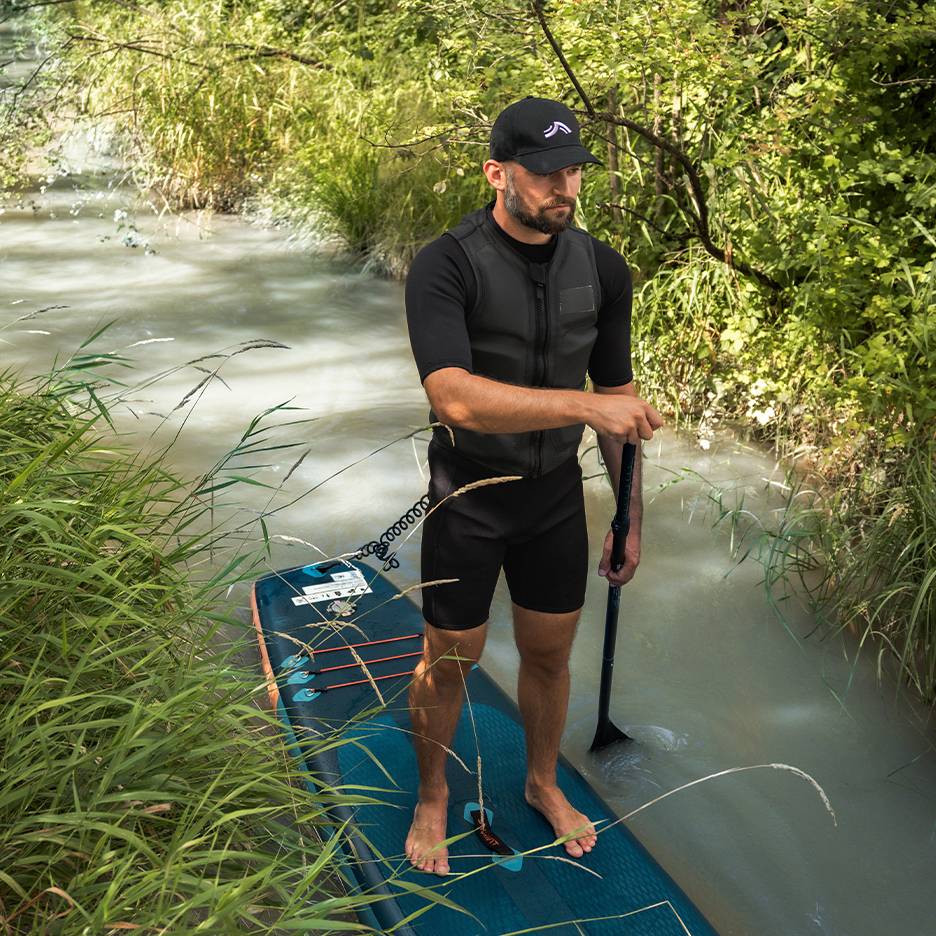 Mann auf einem SUP-Board im Fluss, trägt Neoprenanzug und Schwimmweste.