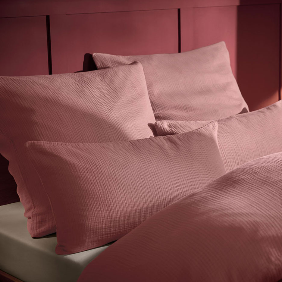 Rosa Musselin-Kissen und Bettwäsche auf einem Bett mit Holzkopfteil.