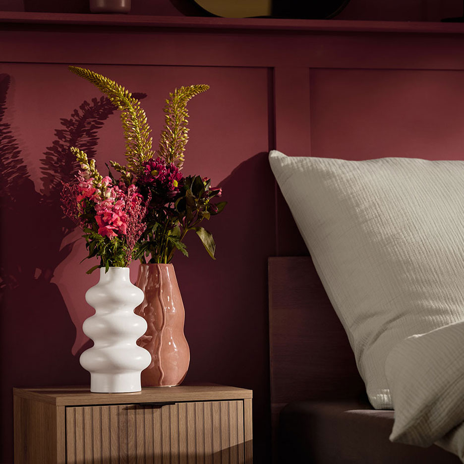 Zwei Vasen mit Blumen auf einem Nachttisch neben einem Bett mit weißem Kissen.